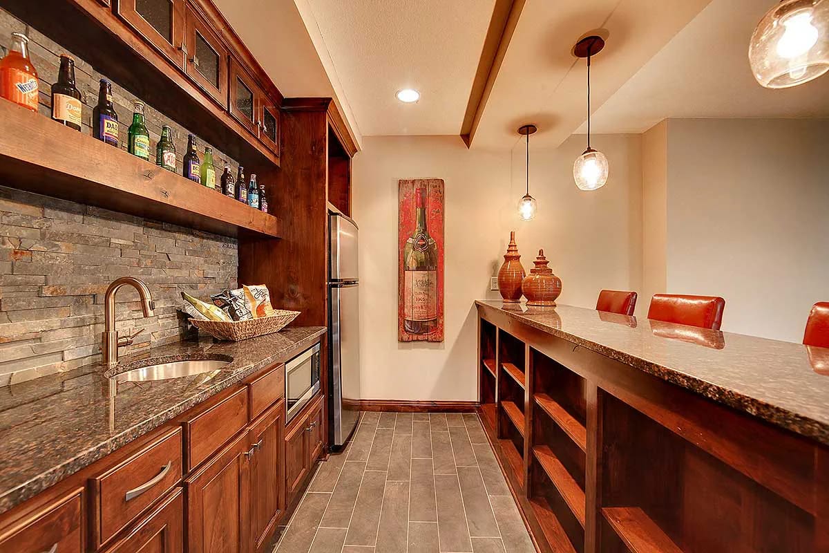 Warm-toned home bar with granite counters, stone backsplash, wood cabinetry, and pendant lights