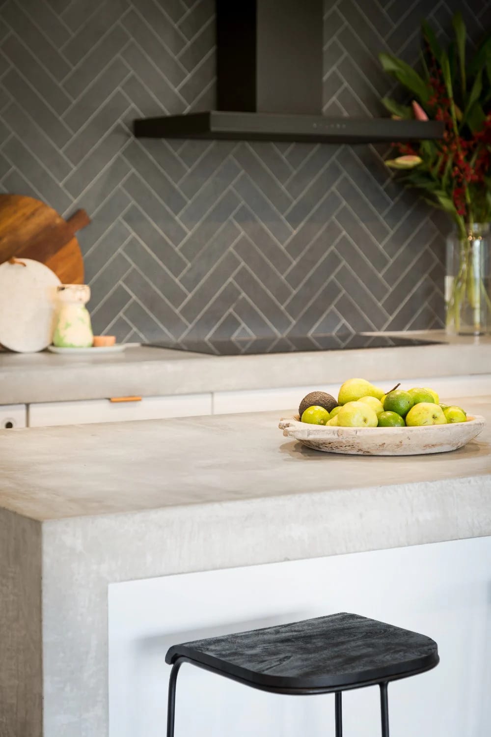 Warm Veined Stone Off-White Kitchen Counter Off-white kitchen with a warm stone countertop, gray herringbone backsplash, black range hood, fruit bowl, and black stool, illustrating a warm off-white kitchen idea