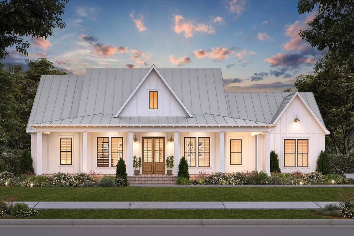 3-Bedroom Modern Farmhouse House Plan with a Wraparound Porch and Home Office (2,085 Sq. Ft. Floor Plan) 1 White cottage-style home with metal roof, centered porch entry, warm windows, and landscaped front garden at dusk
