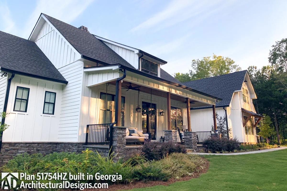 White farmhouse with dark gabled roofs, stone porch piers, and a covered outdoor living area White farmhouse with dark gabled roofs, stone porch piers, and a covered outdoor living area