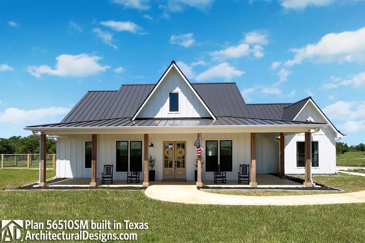 White farmhouse with dark metal roof, broad covered porch, central gable, and rocking chairs White farmhouse with dark metal roof, broad covered porch, central gable, and rocking chairs