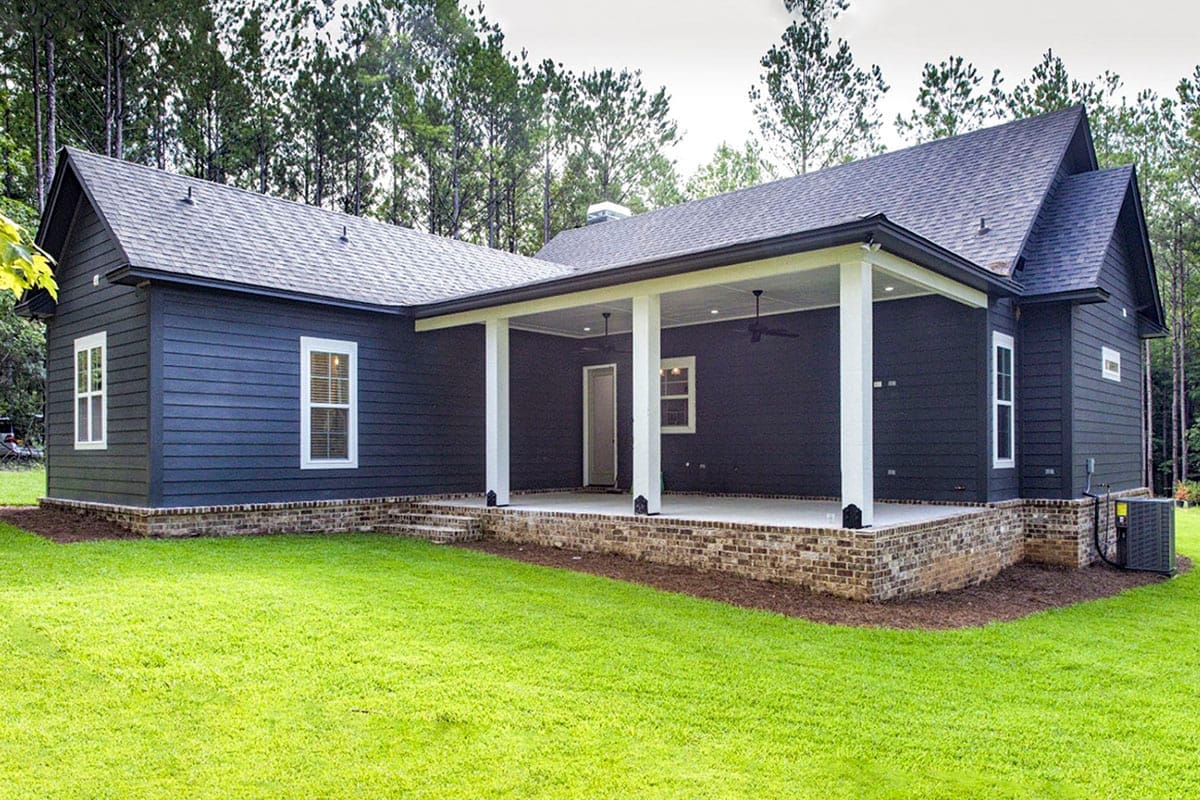 Rear exterior of a dark-sided home with a covered porch, white columns, brick foundation, and gabled roofs Rear exterior of a dark-sided home with a covered porch, white columns, brick foundation, and gabled roofs