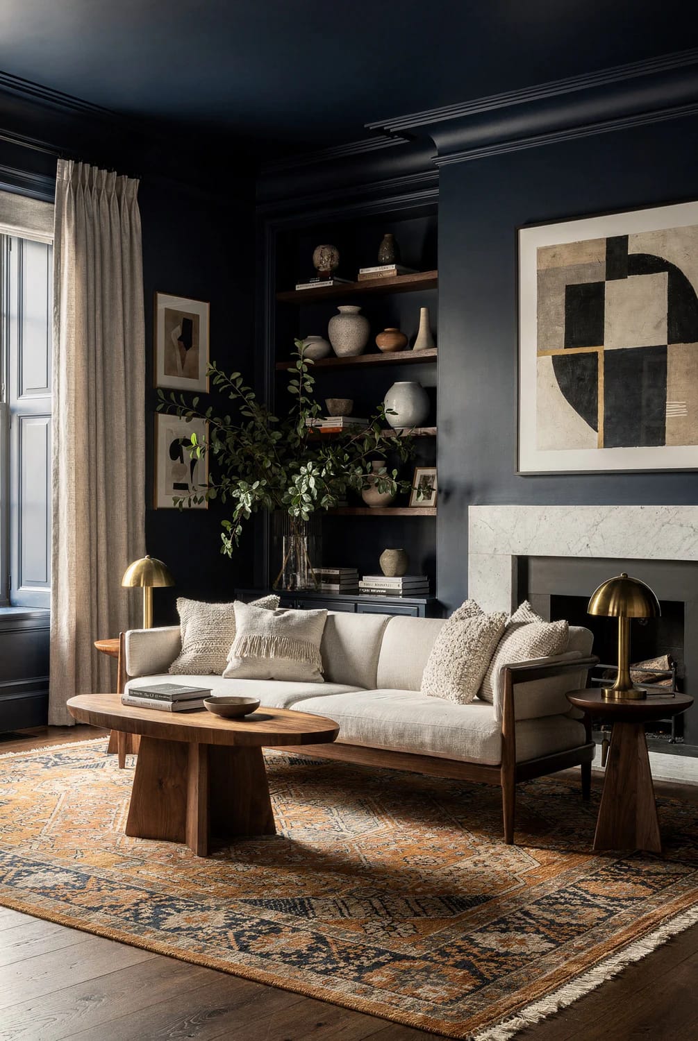 Elegant living room with dark walls and ceiling trim, built-in shelves displaying pottery and books, a cream sofa with textured pillows, a wooden coffee table, brass lamps, a patterned rug, artwork, and a fireplace.