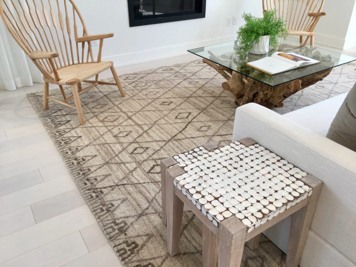 Rich living room featuring two spindle-back wood chairs, a white sofa, a large geometric area rug, a glass-top driftwood coffee table with greenery, and a textured wooden stool.