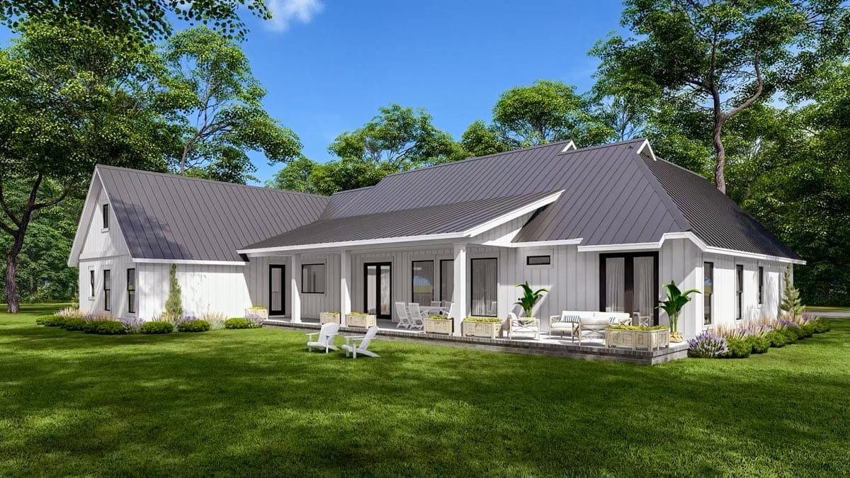 Single-story white-sided home with dark metal gables and a furnished covered patio in a wooded setting