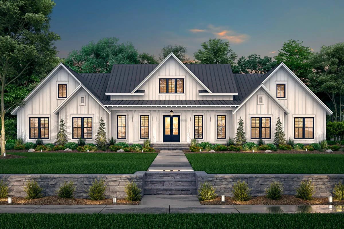 Symmetrical white farmhouse exterior with dark metal roofs, central porch, stone wall, and landscaped walkway