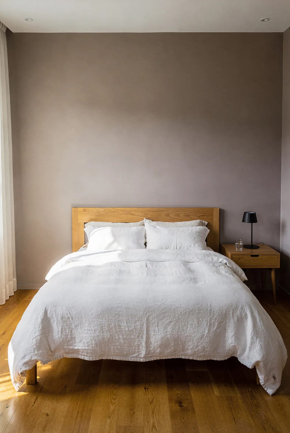 Warm Neutrals With Orange Wood Floors Bedroom with warm taupe walls, an orange-toned wood floor, a wooden bed frame, white bedding, and a wooden nightstand with a black lamp, illustrating warm neutrals that work with wood floors